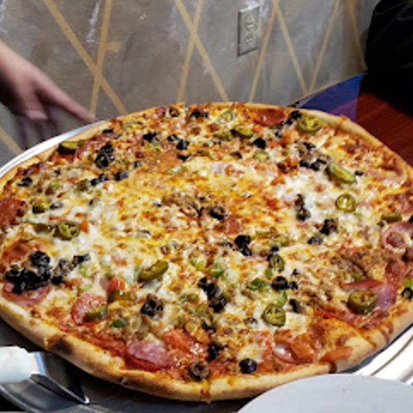 A large, round pizza with various toppings including pepperoni, olives, and jalapeños, on a metal tray.