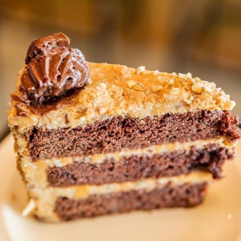 Slice of chocolate cake with peanut butter frosting and a dollop of chocolate on top.