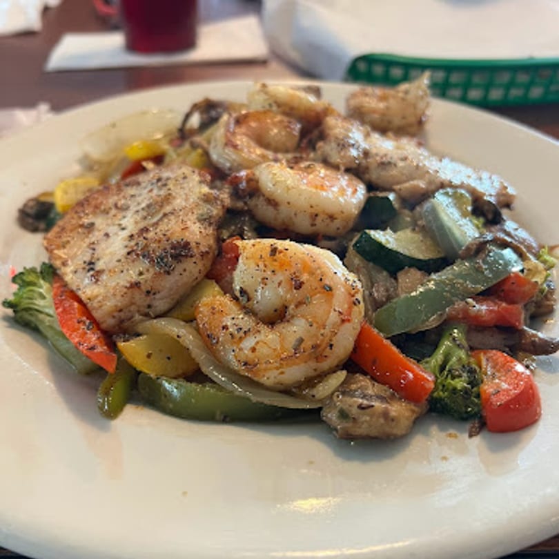 Grilled chicken and shrimp with sautéed bell peppers, onions, zucchini, and broccoli on a white plate.