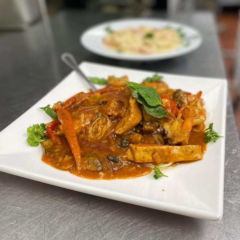 Italian seafood pasta dish with shrimp, chicken, vegetables, and a creamy orange sauce, garnished with basil and parsley.