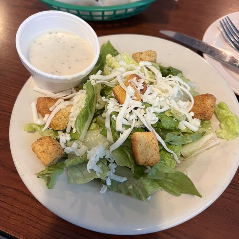 A side salad with lettuce, shredded cheese, croutons, and a cup of ranch dressing.